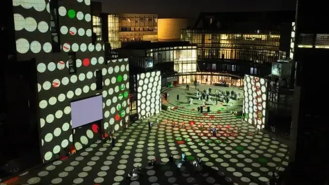 Beleuchtetes Landtagsgebäude in Düsseldorf mit kreisförmigen Lichtprojektionen in Weiß, Rot und Grün auf Fassaden und Vorplatz.