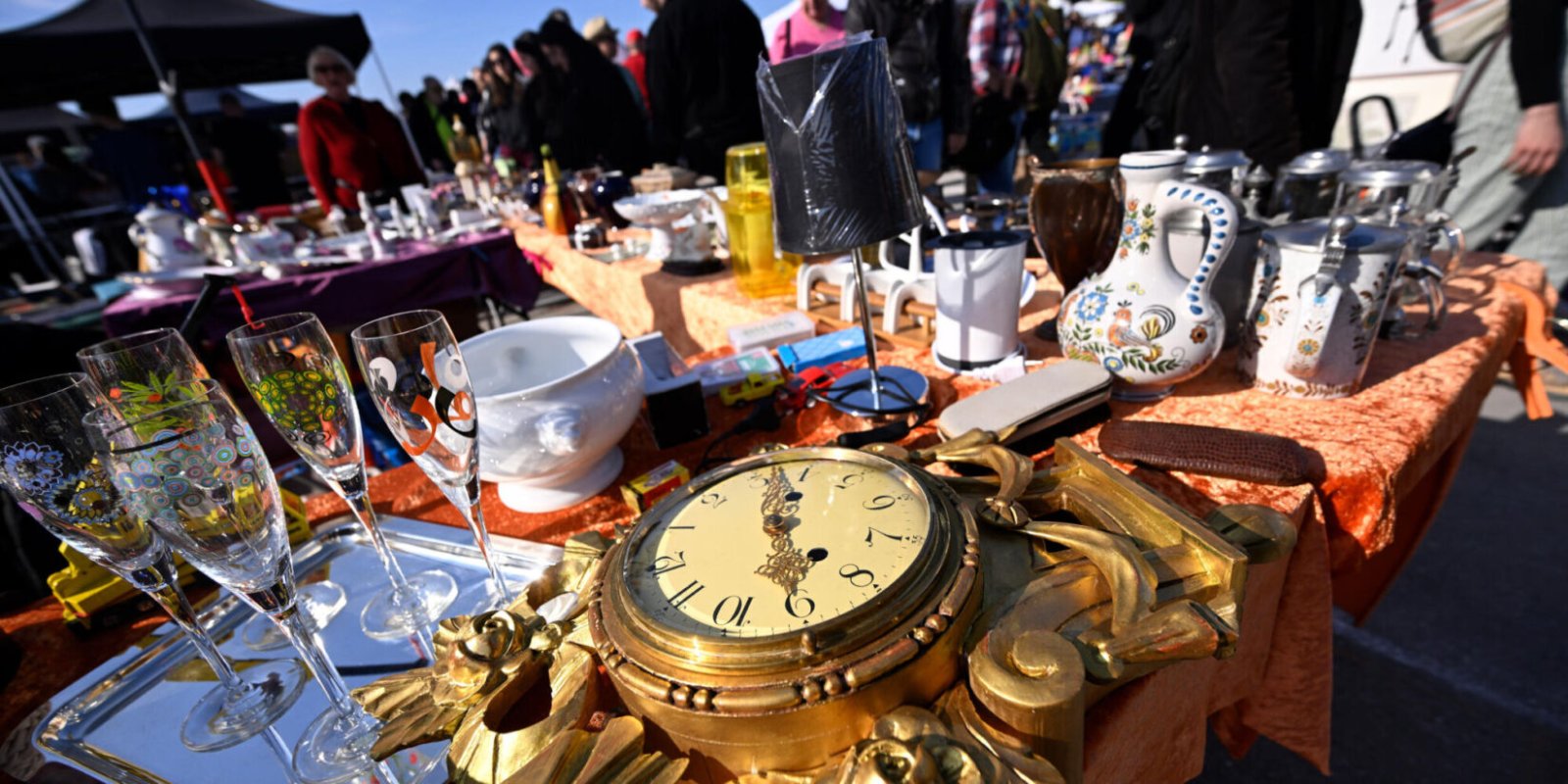 Ein Tisch auf einem Trödelmarkt mit einer alten Uhr, Sektgläsern und Porzellan.
