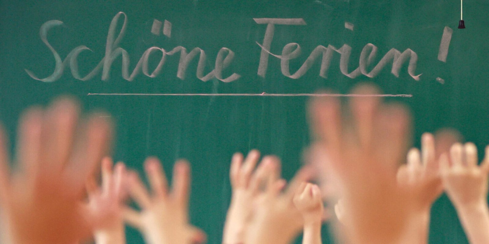 „Schöne Ferien!“ steht auf einer Tafel in einem Klassenraum, in dem die Schüler vor Freude die Hände heben.